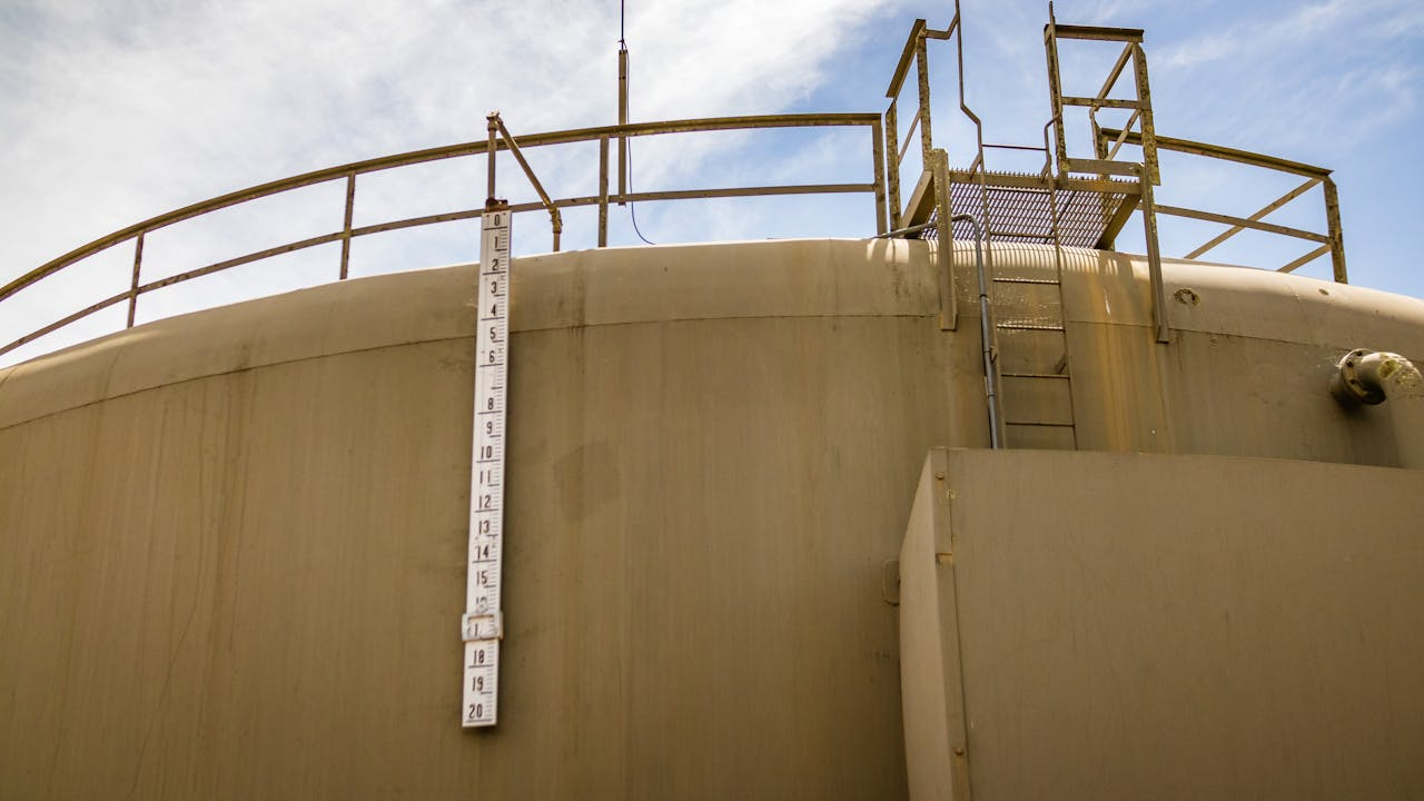 A low angle view of a large industrial water tank with a measuring scale and ladder under a clear sky.